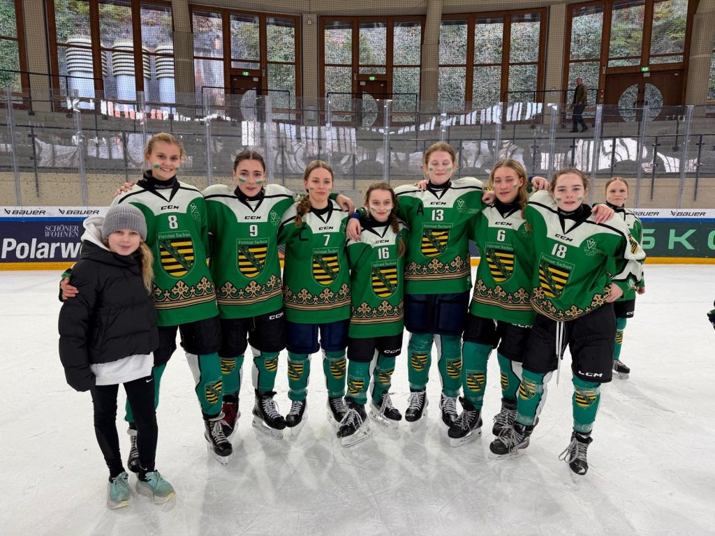 Gruppenbild der Berliner Eishockey-Nachwuchsspielerinnen in grünen Trikots auf dem Eis vor der Bande